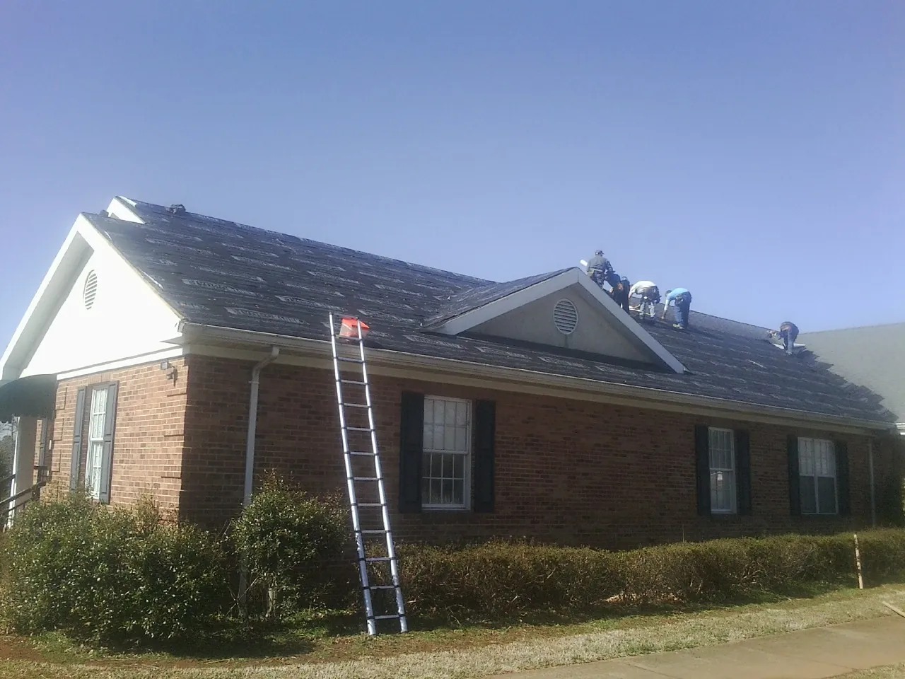 Crew tearing shingles off a brick ranch roof with a ladder set — Metal Roof Repair work by our crew in Coleman