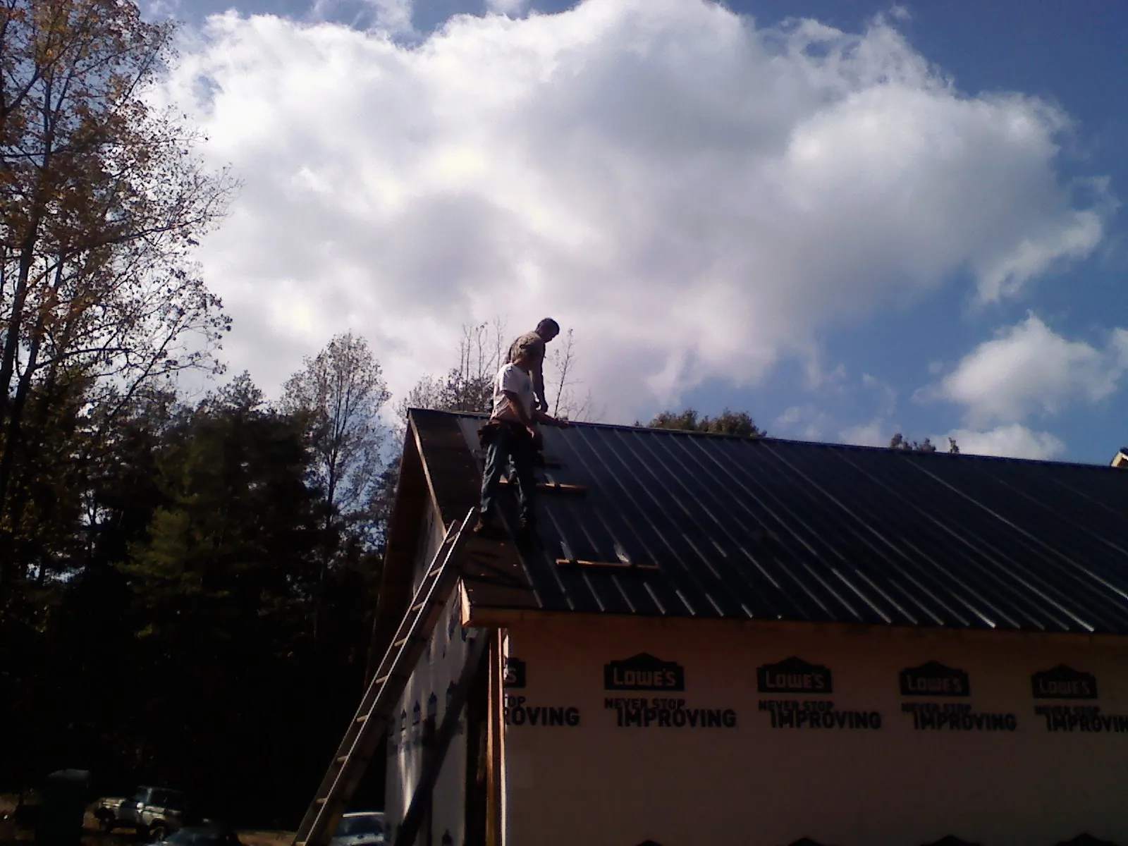 Roofer fastening dark metal panels high against a cloudy sky, from a Roof Inspection job in Coleman