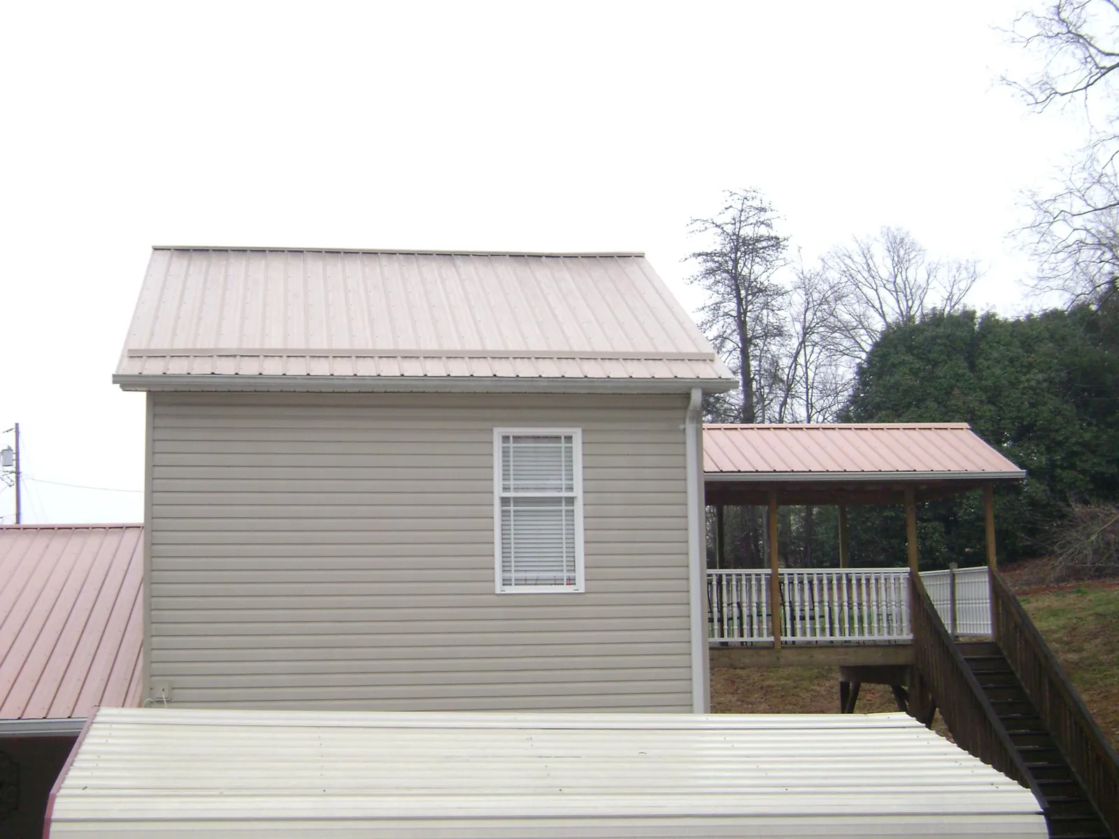 Tan metal roofs on a two story addition and attached porch, from a Roof Replacement job in Coleman